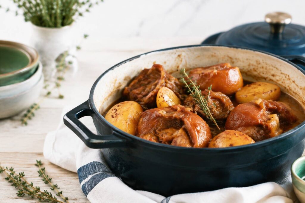 Plat mijoté de queue de cochon en cocotte en fonte avec pommes de terre sur table en bois