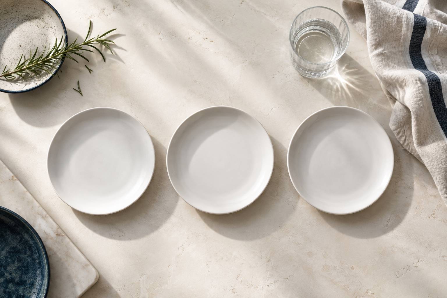 Trois assiettes vides alignees et verre d'eau sur une table claire